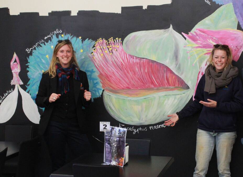 Christina Laue (left) with the mural she painted on the wall of the Wheatbean Café, with Sarah Gilleland, who named the popular meeting place in Perenjori.