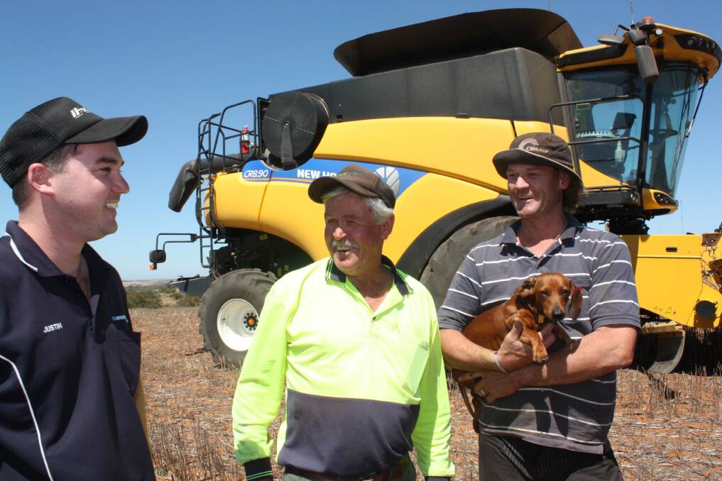  McIntosh & Son salesman Justin Clarkson (left), talks with Ogilvie farmers Alan and Rhys Carson (holding dog Bailey) about the performance of their New Holland 8.90 combine harvester. 