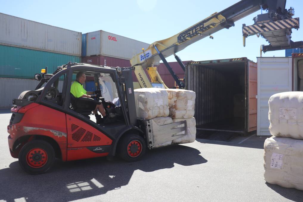 Wool bales being loaded into a container in the yard at IWD Pty Ltd. The stack of containers in the background is loaded with wool and should have already gone but was delayed by changes to shipping schedules.