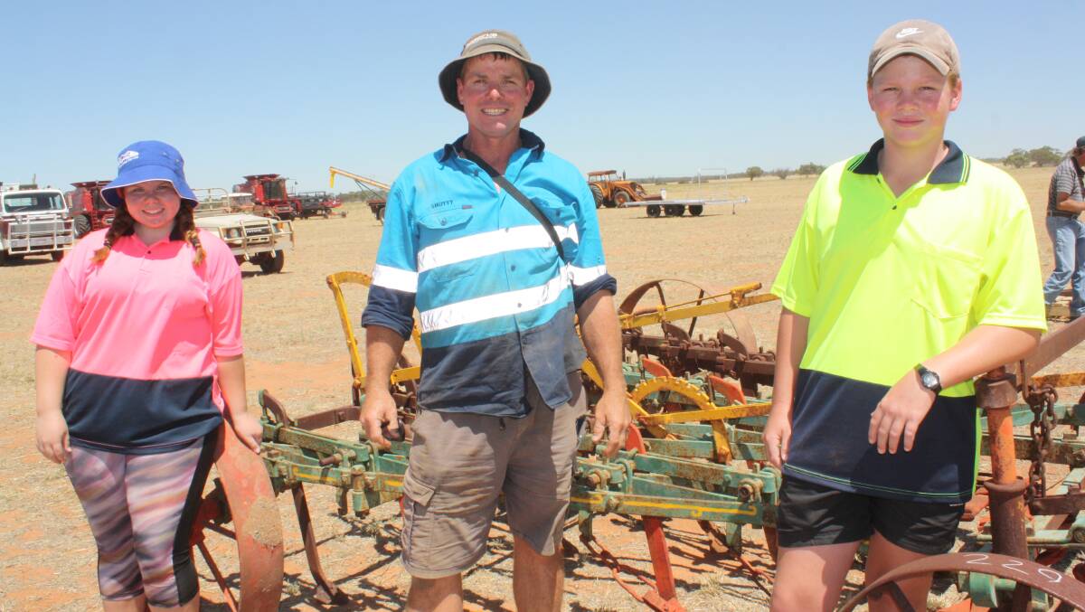 Aaron Smith maintained a positive smile with his daughters Jordi (left) and Bailey as he helped his father Steve organise the sale. “I'll be staying in the district to keep on farming,” he said. The horse-drawn scarifier the trio are pictured in front of was knocked down for $50 to a keen collector.