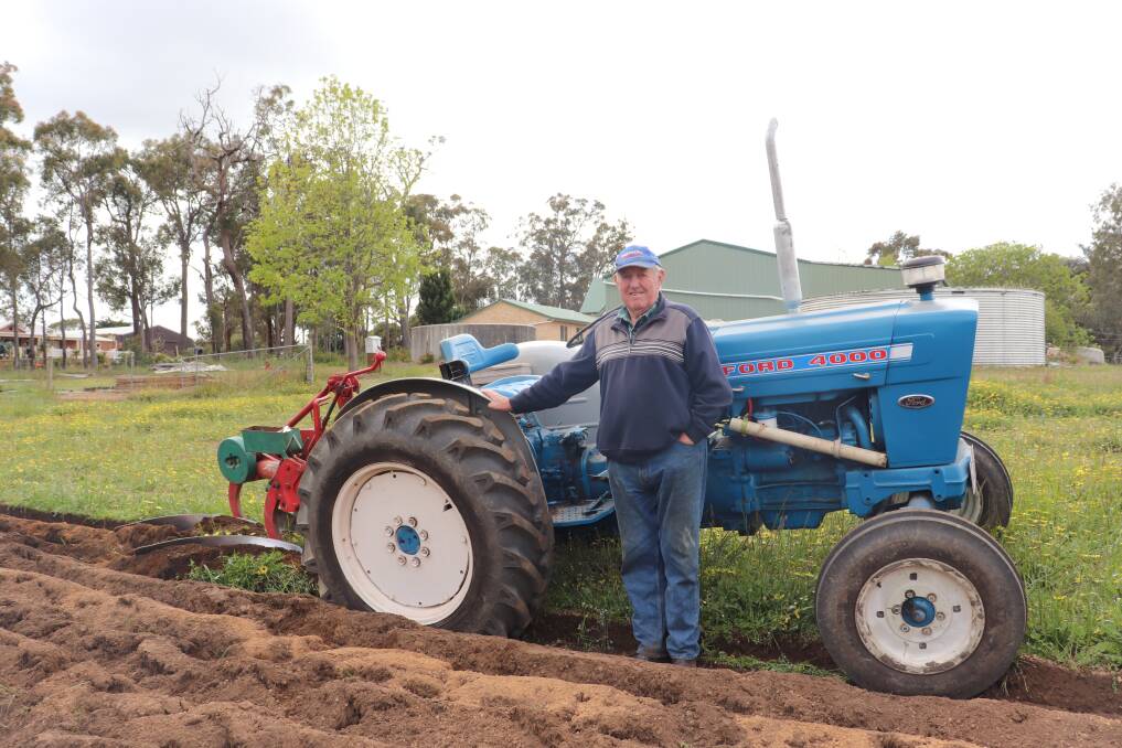 Mr Richings in front of his bright blue 1960-70s 42.5 kilowatt (57 horsepower) Ford 4000, fitted with a mouldboard plough at the back.